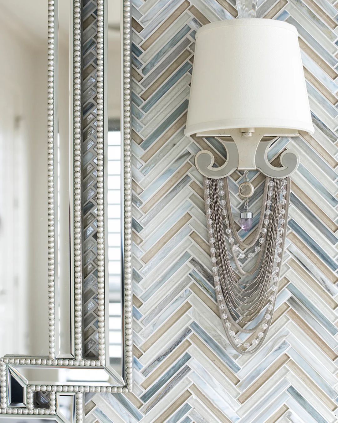 Herringbone tile wall with mirror, sconce, and beaded embellishment.