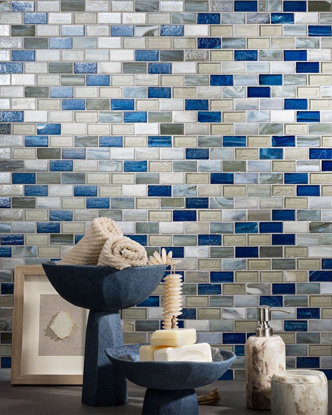 Blue, gray, and white mosaic tile bathroom wall with toiletries and decorative items.