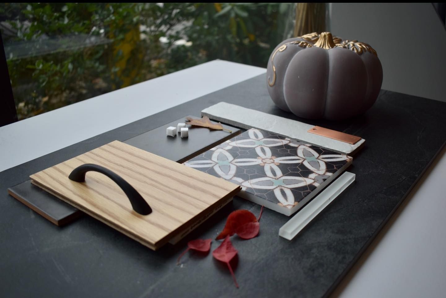A pumpkin sits on a table next to a tray of wood and tiles