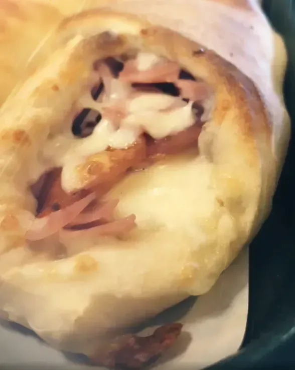 Close-up of a pastry roll filled with melted cheese and ham.