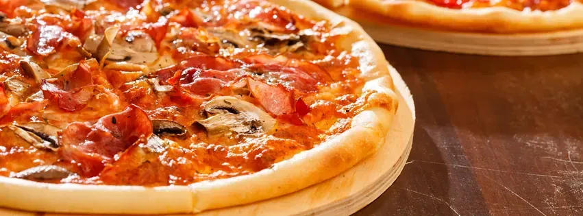 Two pizzas on wooden serving boards, topped with sauce, mushrooms, and meat.