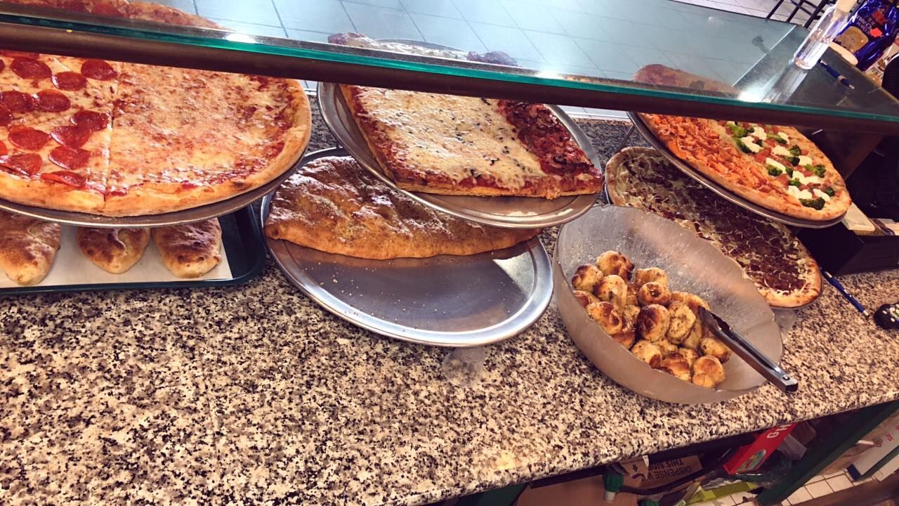 Pizzas and breaded items displayed behind a glass counter at a restaurant.