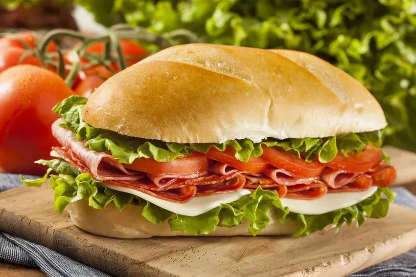 Submarine sandwich with salami, cheese, lettuce, and tomato on a wooden board.
