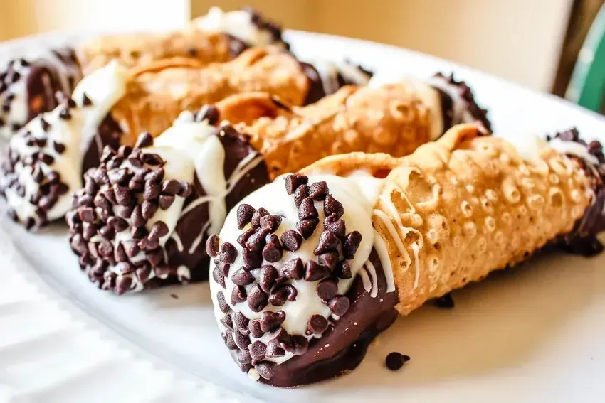Cannoli pastries arranged on a white plate, some dipped in chocolate and covered in mini chocolate chips.