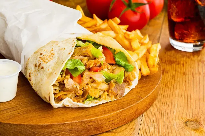 Wrap of meat, vegetables, and sauce with fries, tomatoes, and a drink.