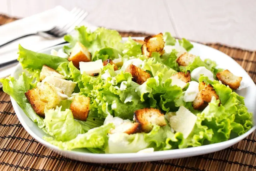 Caesar salad: Romaine lettuce, croutons, parmesan cheese, on a white plate.