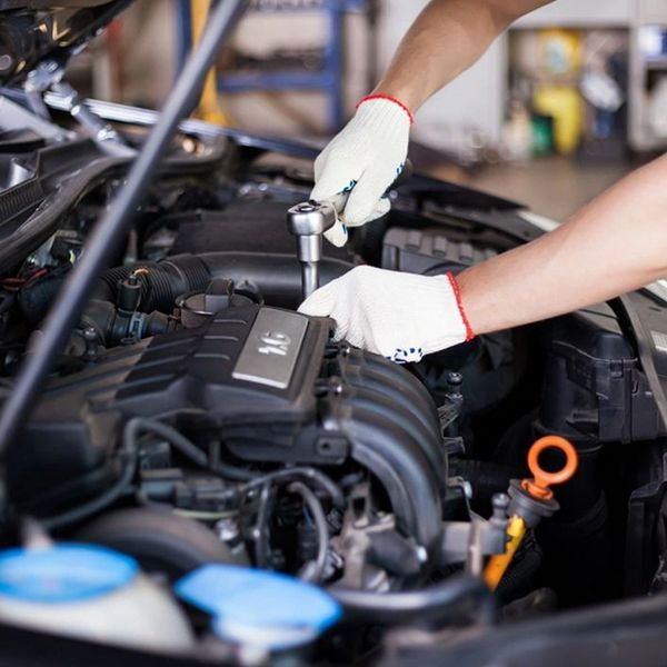 Mechanic working on a car engine with a wrench, wearing gloves in a garage.