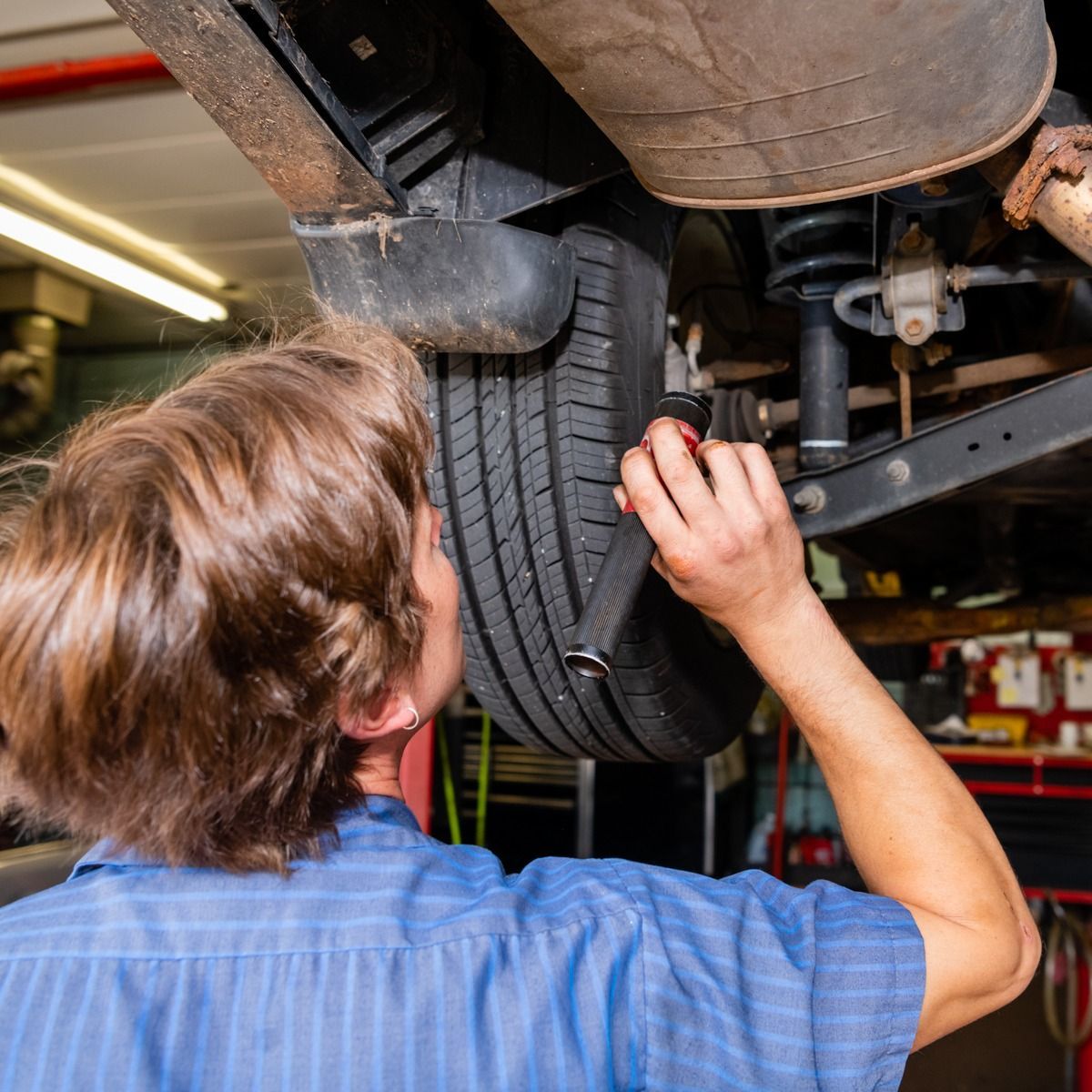 Mechanic inspecting a car tire from underneath, in a garage.
