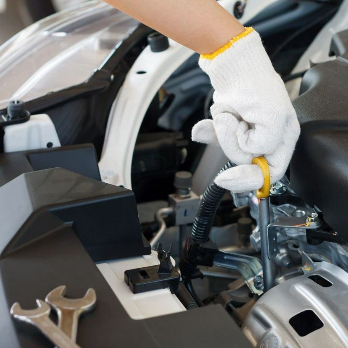 Mechanic checking car engine oil with dipstick, wearing white glove, tools visible.
