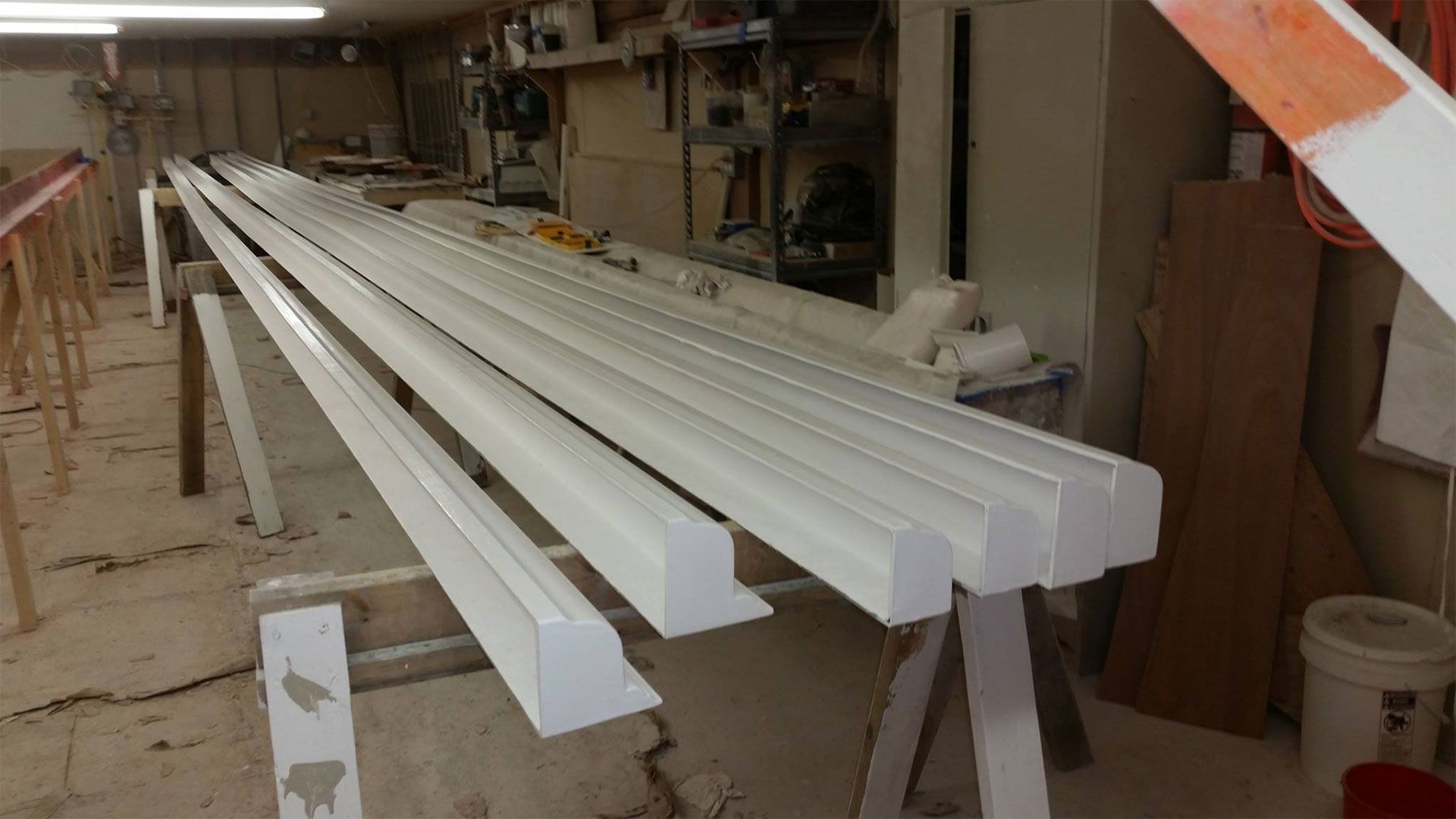 White painted molding pieces drying on sawhorses in a workshop.