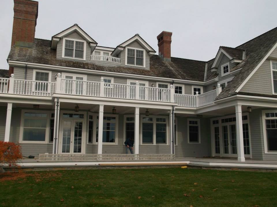 Large gray house with multiple stories, balconies, and dormers. Brick chimneys and overcast sky.