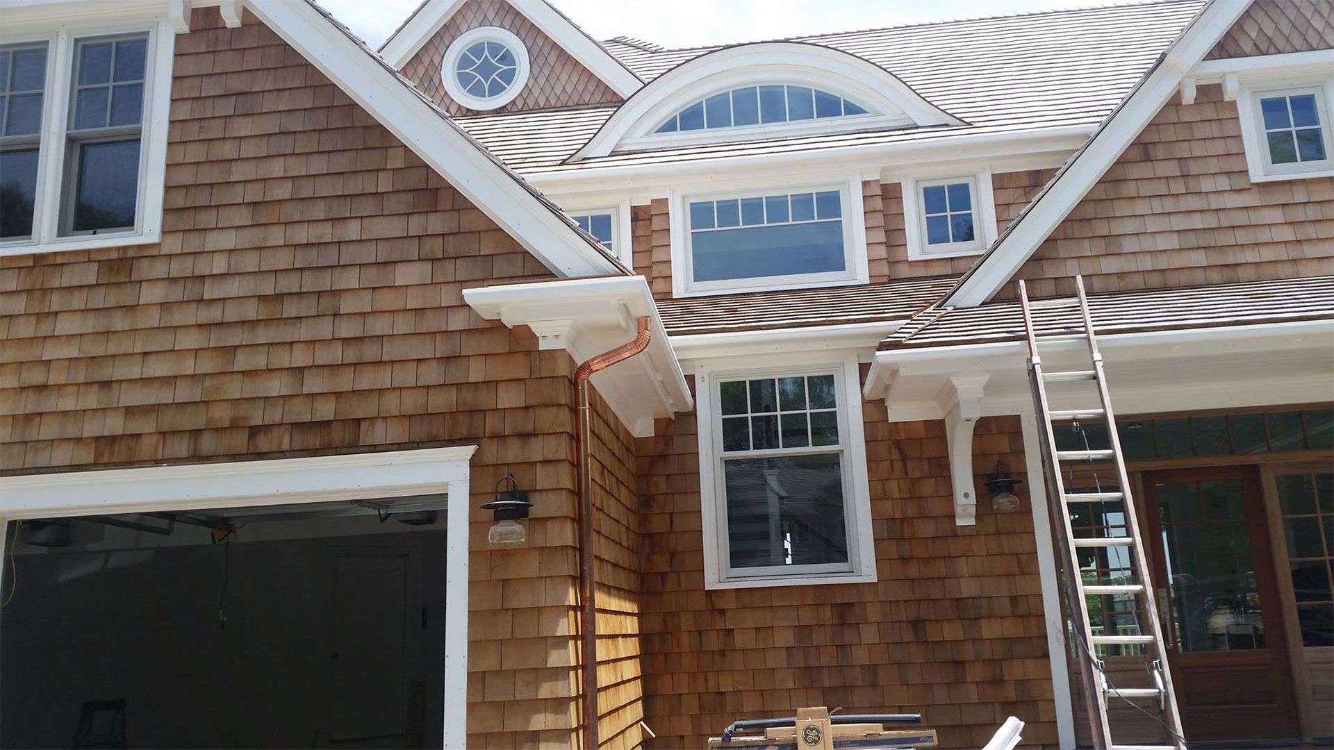 Exterior view of a house with brown cedar shake siding, white trim, and a ladder leaning against the side.