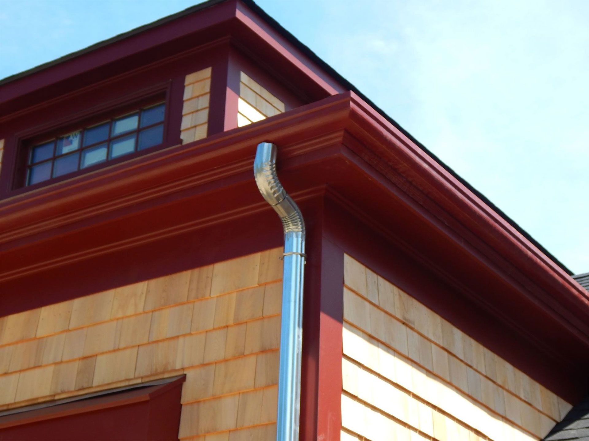 Red trimmed building with wooden shingles, silver gutter and downspout.