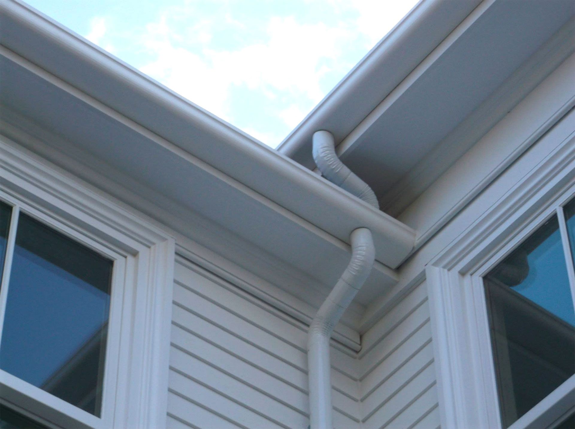 White gutters and downspout on a house with white siding and windows.