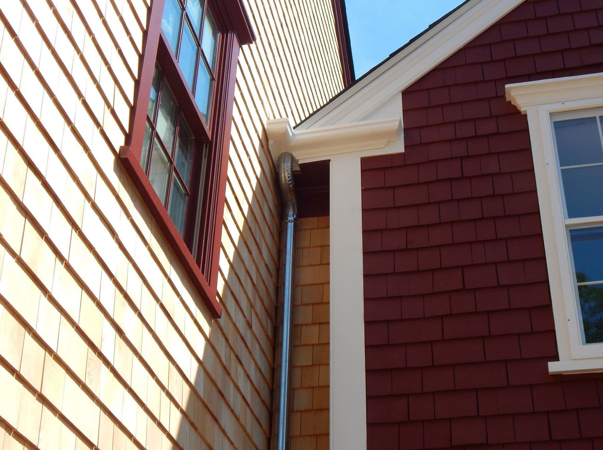 Two buildings with different colored siding connected by a downspout.