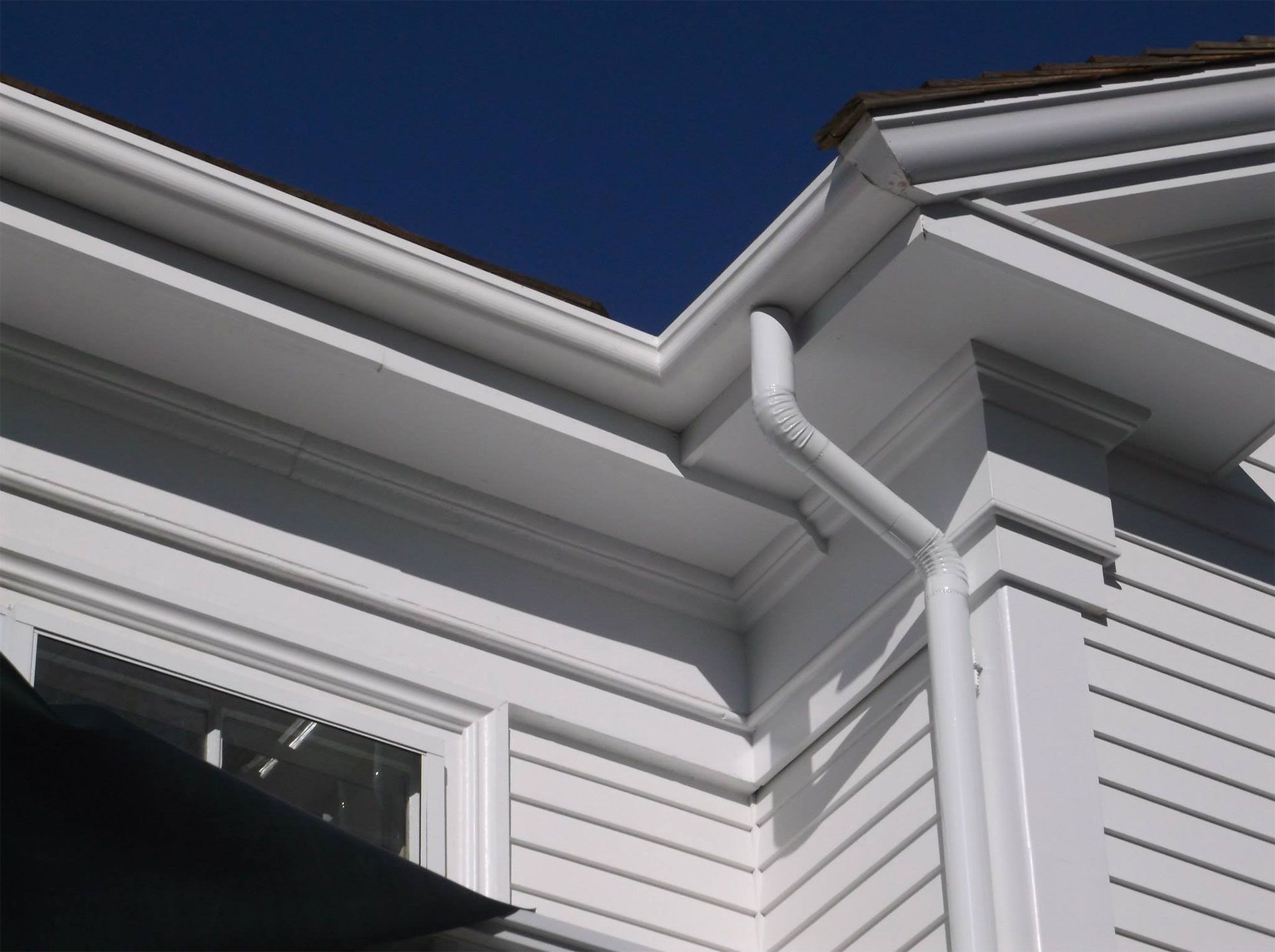 White house exterior with gutters and downspout against a blue sky.