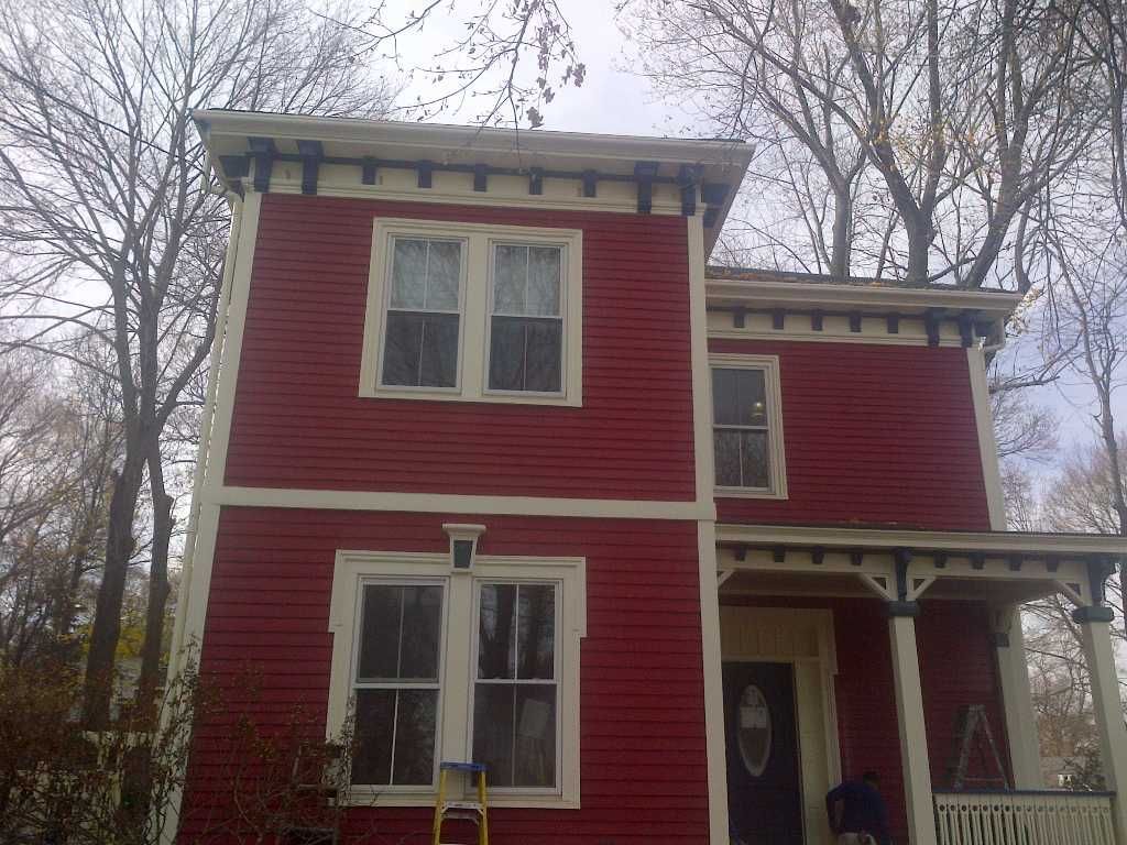 Red two-story house with white trim. The house has a porch and several windows, with bare trees in the background.