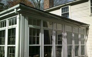 Sunroom addition with white-framed windows, attached to a house with white siding and a chimney.
