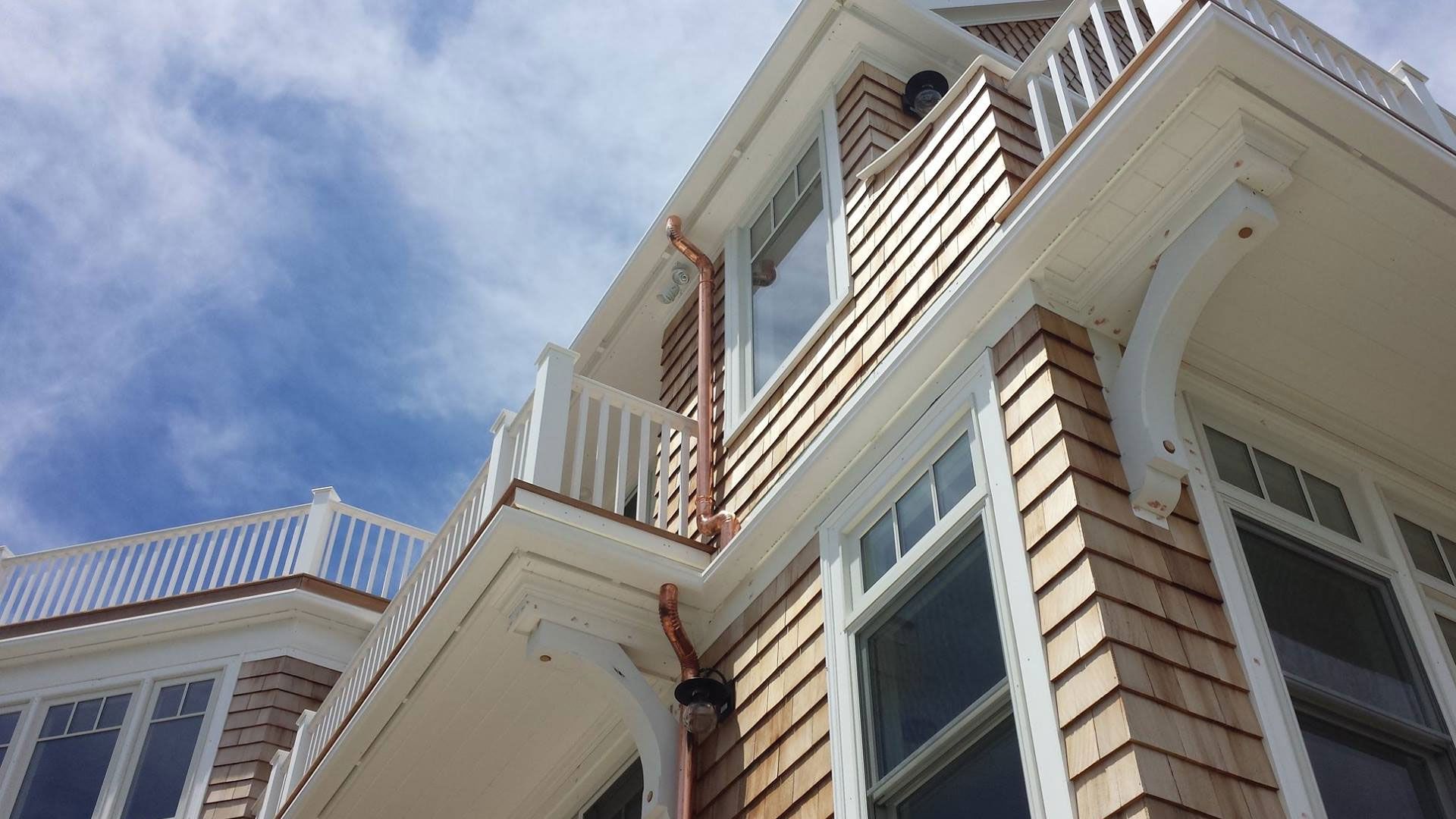 Building exterior with wood shingles, white trim, and copper gutters, against a blue sky.