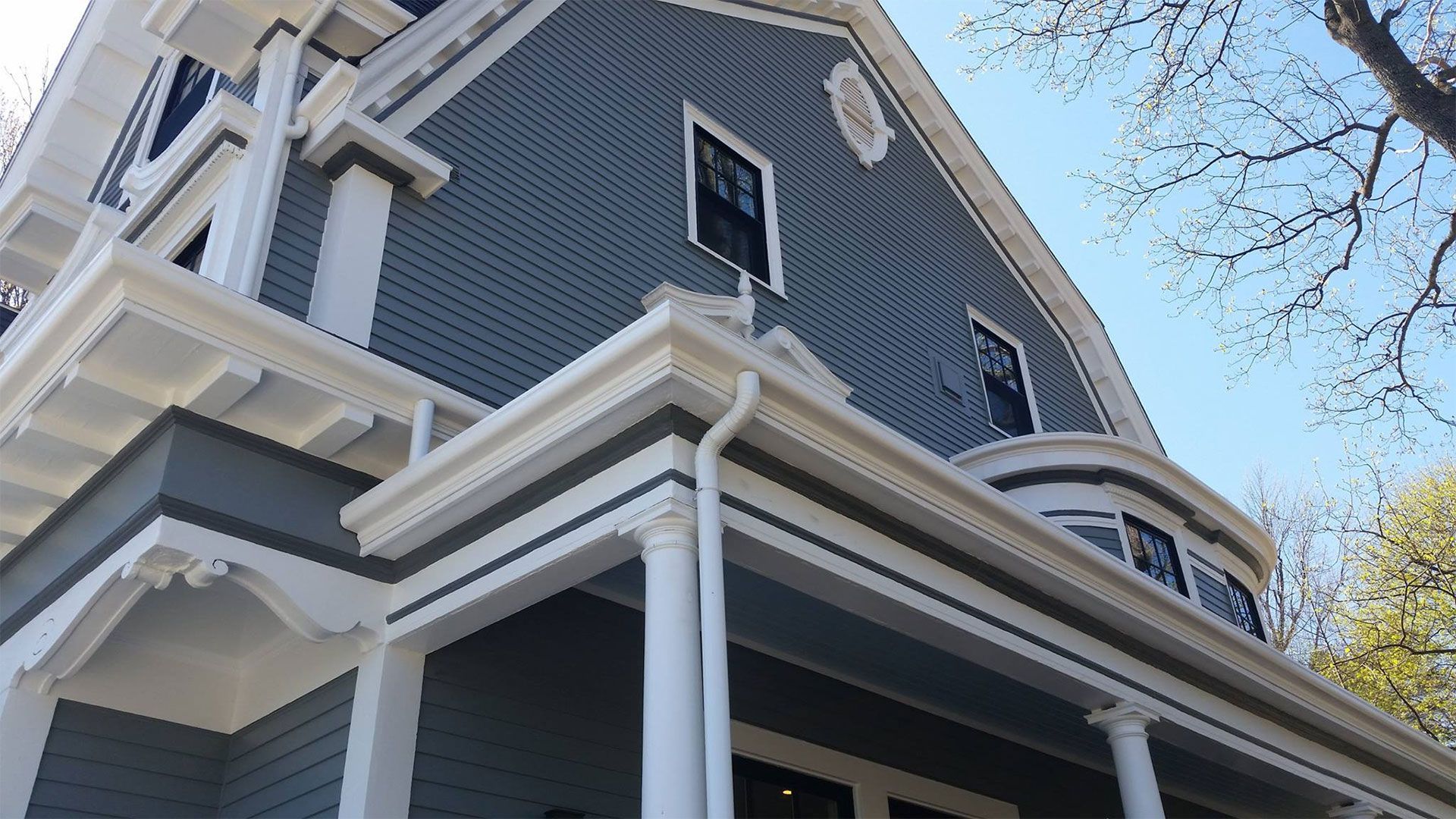 Gray and white Victorian house with porch and ornate trim, under a sunny sky.