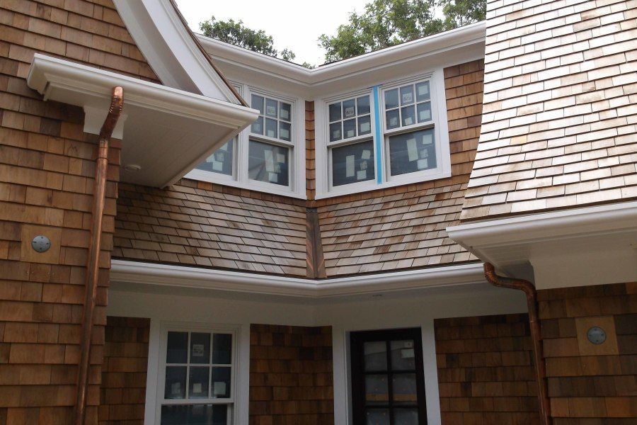 Brown shingle siding and roof on a house with white trim, windows, and copper gutters.