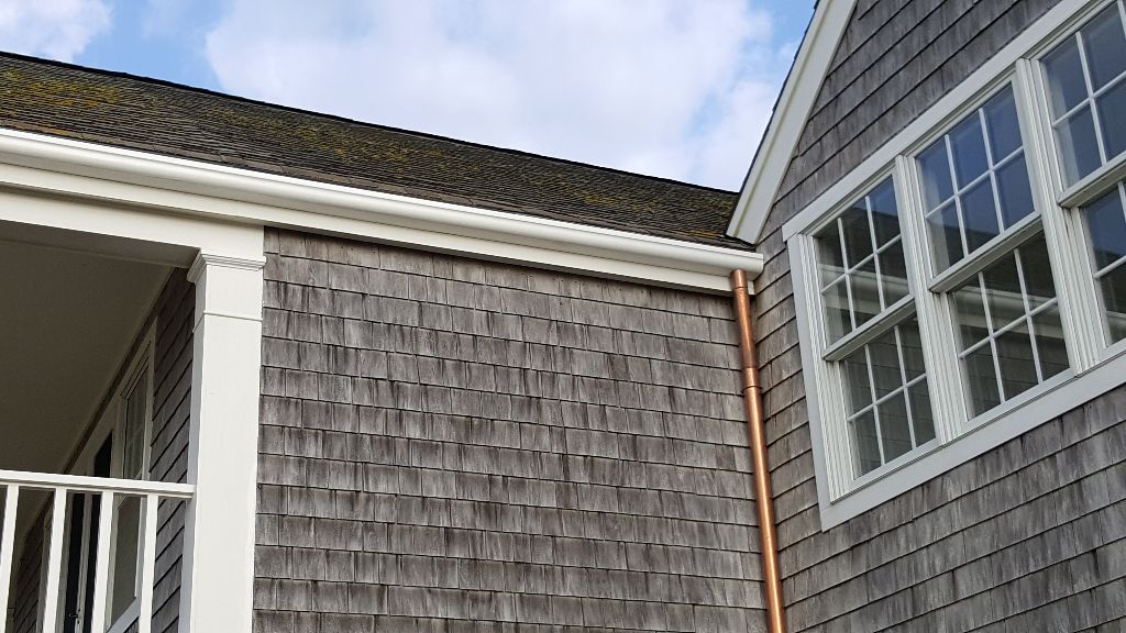 Exterior of house with weathered shingles, white trim, copper gutter, and windows.