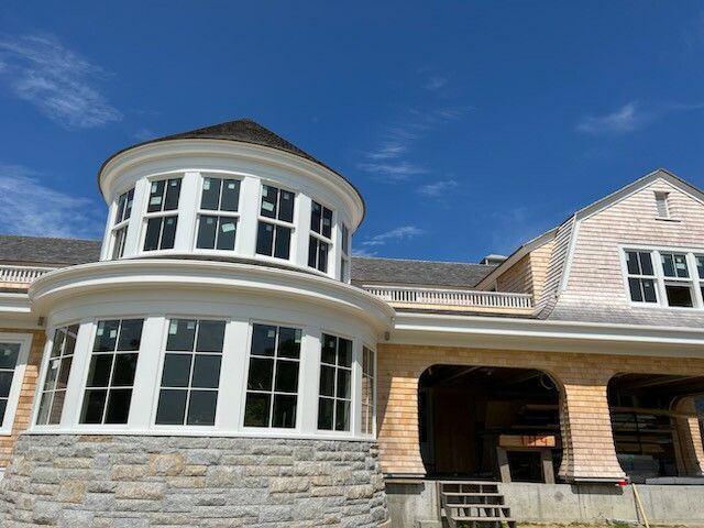New coastal home under construction with a round tower and light wood shingles.