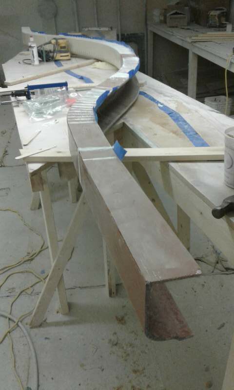 A curved, unfinished wooden architectural element on sawhorses in a workshop.