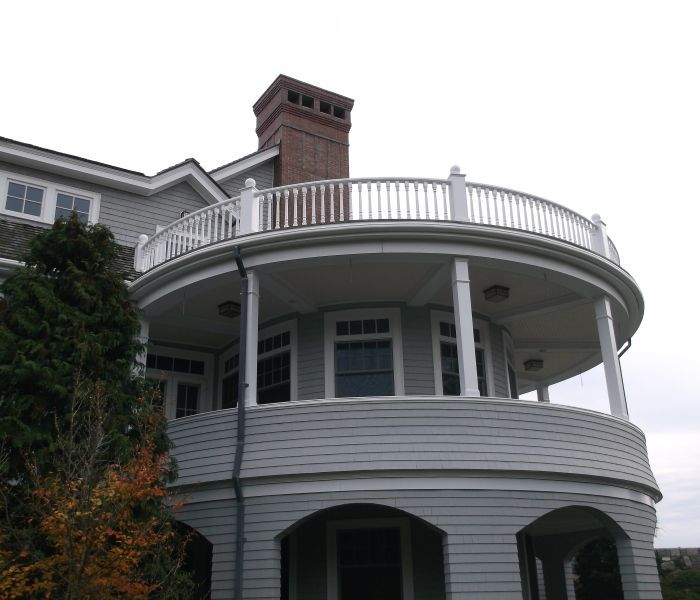 Gray house with a circular balcony and white railing, brick chimney.