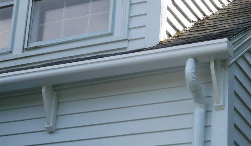 White house exterior with light blue siding, gutters, and window.