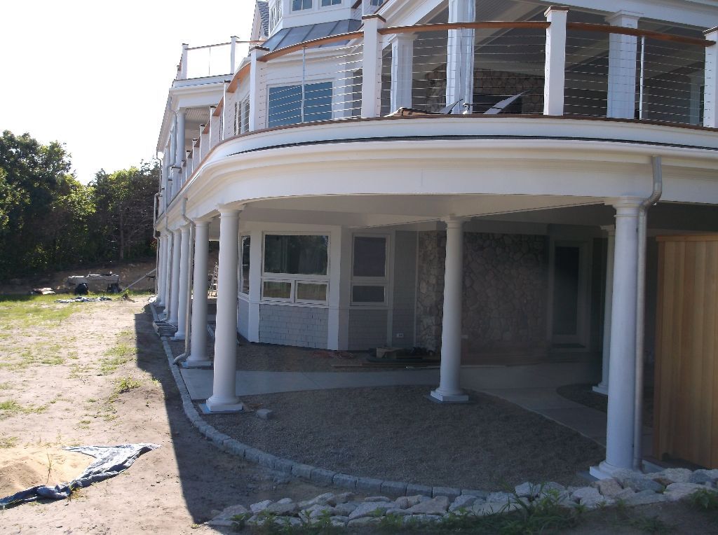 White multi-story house with columns and a wraparound porch, gravel pathway in foreground.