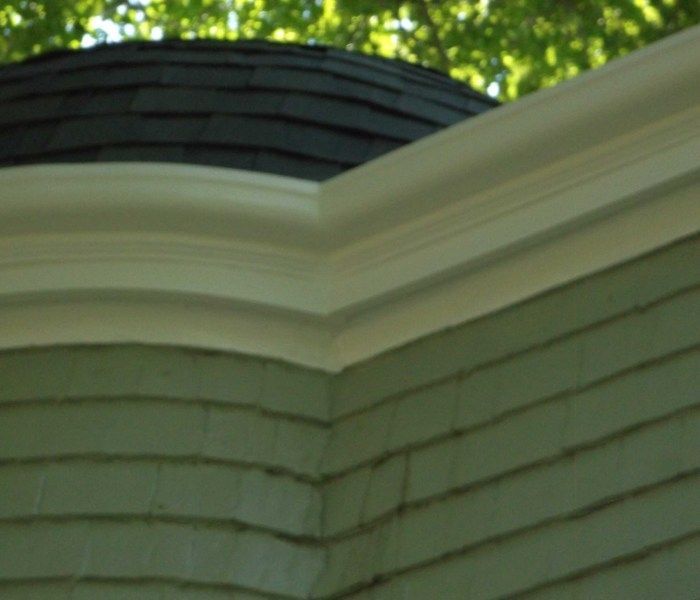 Close-up of a house corner with light green siding and white trim. Dark roof in background.
