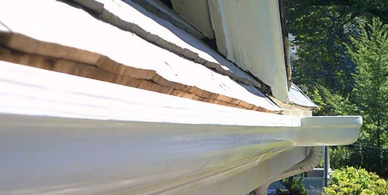 Close-up view of a white gutter attached to a roof with wooden shingles.