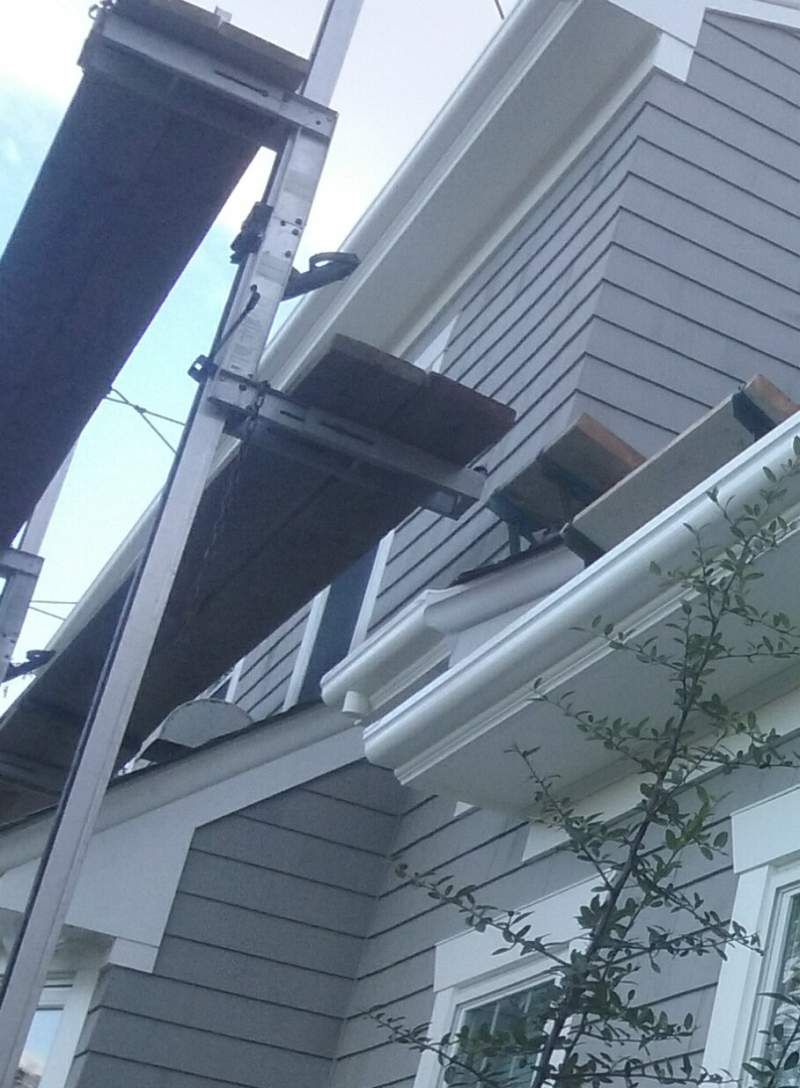 Scaffolding next to a house with gray siding and white trim; gutter installation in progress.