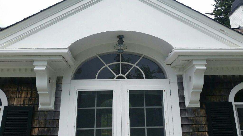 White arched doorway with decorative trim, brackets, and a curved window above.