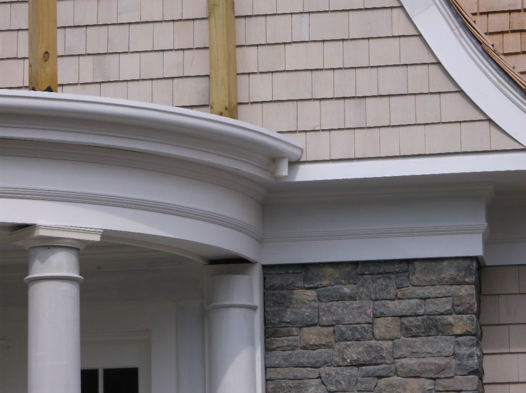 White porch with curved trim, next to a stone wall and shingle siding.