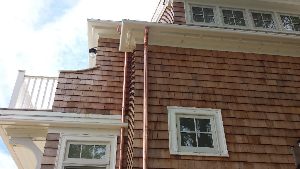 Brown shingled house exterior with white trim, windows, and copper gutters.