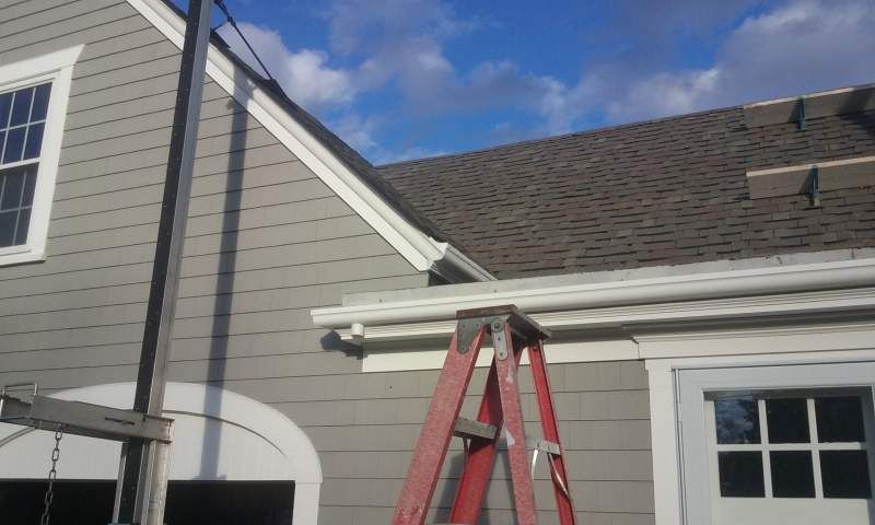 Gray house with a red ladder and a construction hoist, under a blue sky.
