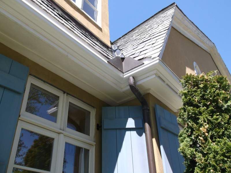 Tan building with a white trim, blue shutters, and a dark brown downspout.