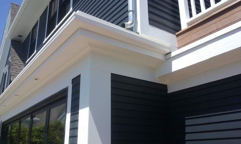 White and dark gray building corner with architectural details, including trim, siding, and gutter.