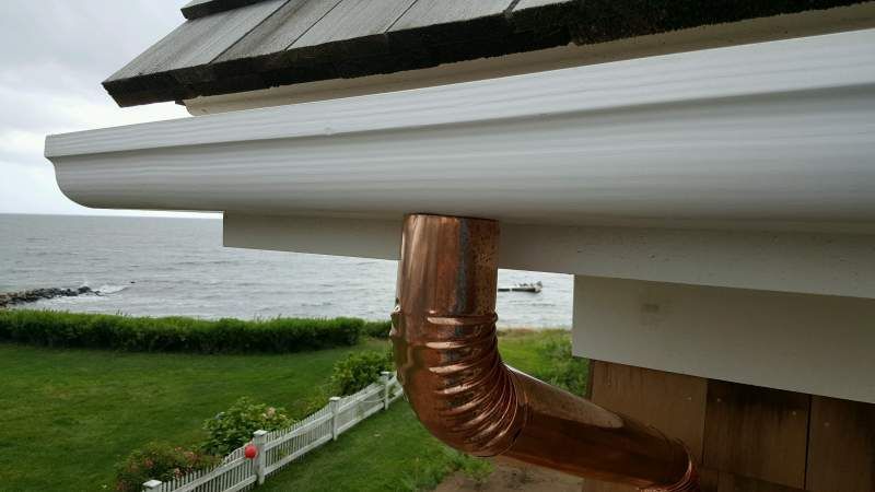 White gutter with copper downspout on a house overlooking a body of water.