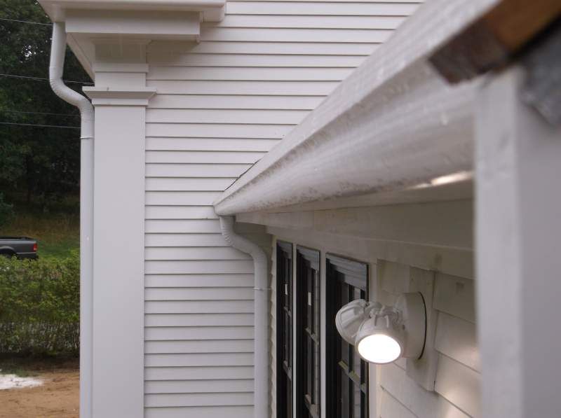 White house exterior with column, gutter, and a lit security light.
