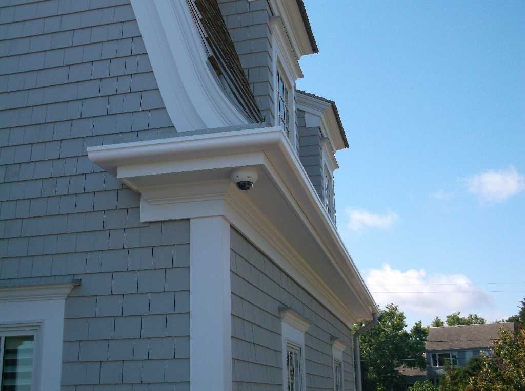 Gray shingled house exterior with white trim, security camera, and blue sky.