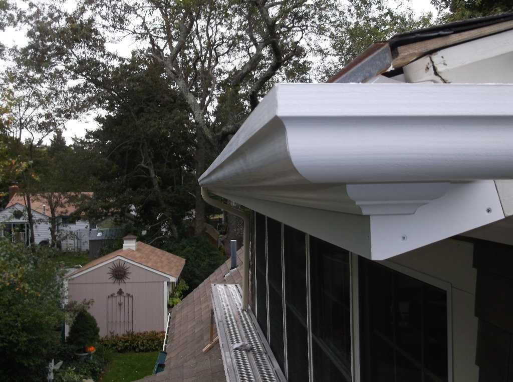 White gutters on a house with a wooded background and a screened porch.