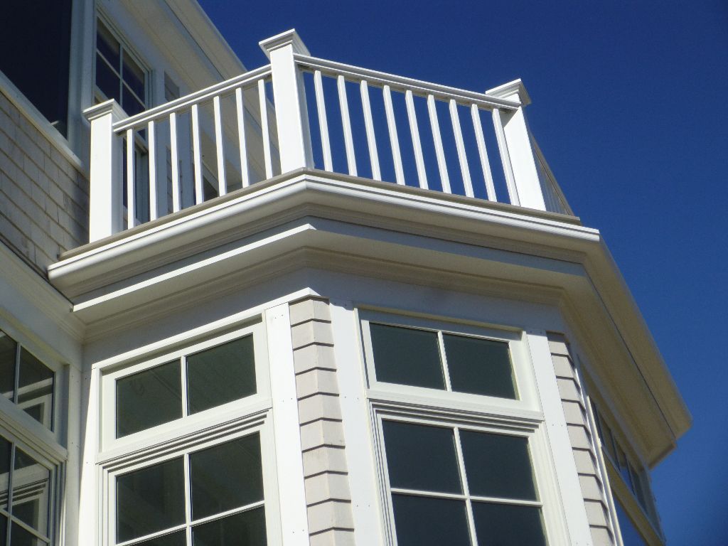 White railing on the roof of a bay window on a building with a blue sky background.