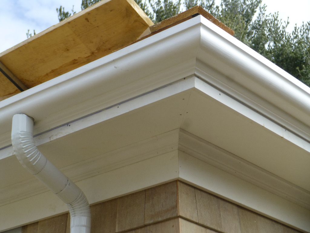 White roofline with gutter and downspout, on a building with brown siding.