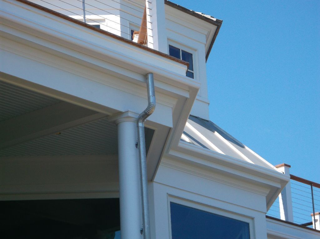 White house exterior with gutter and downspout against a clear blue sky.