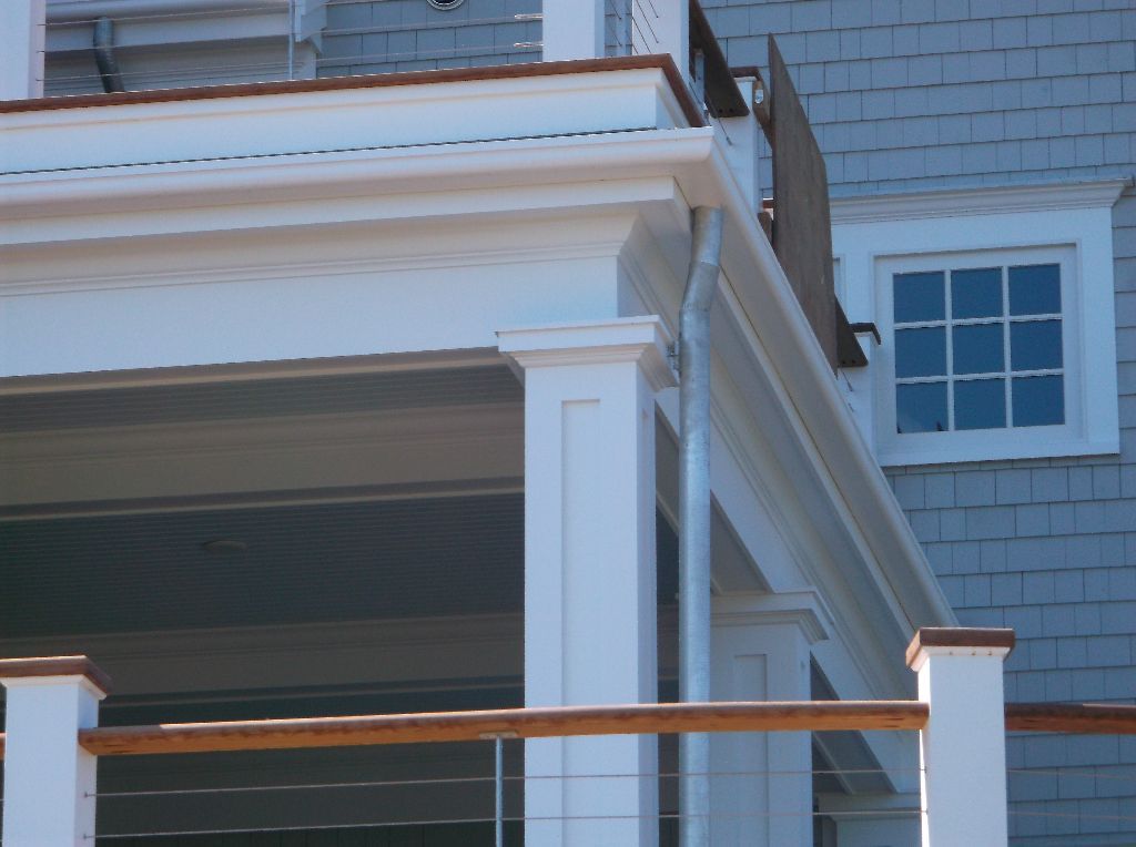 White porch with a column, copper-colored railing, and a window on a gray shingled wall.