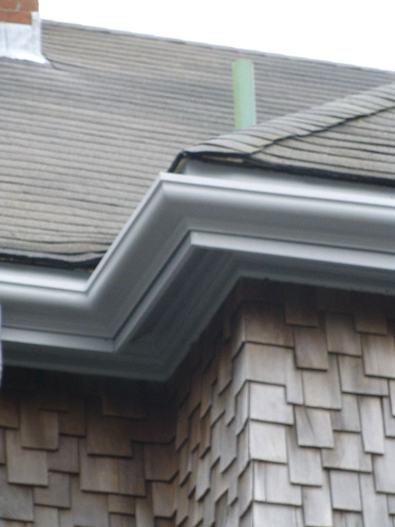 Gray gutters on a building with a shingle facade and roof. A green vent pipe is visible.