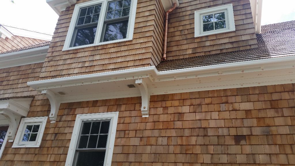 Cedar shingle siding and roof on a house with white trim, windows, and copper rain gutters.